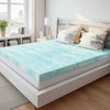 A light blue patterned memory foam mattress topper placed on a white bed frame in a bright bedroom.