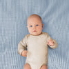 A baby wearing a beige striped onesie lying on a light blue waffle blanket.