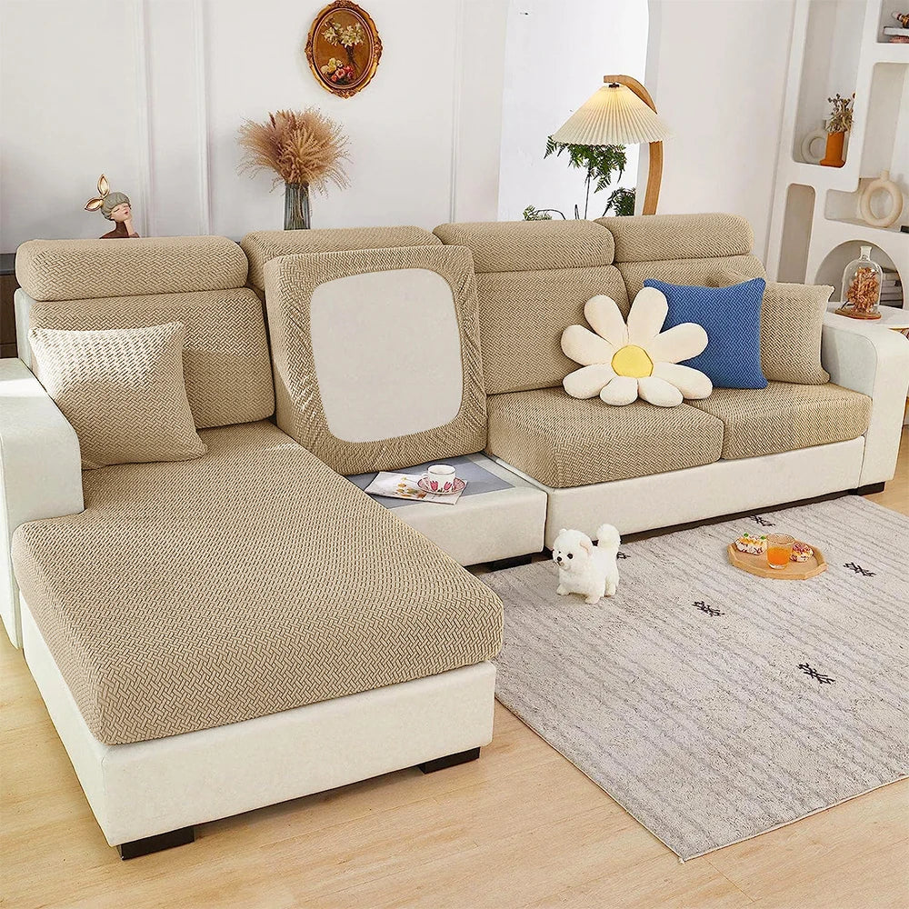 A beige jacquard elastic sofa cushion slipcover on a light-colored sofa with decorative pillows and a white dog.