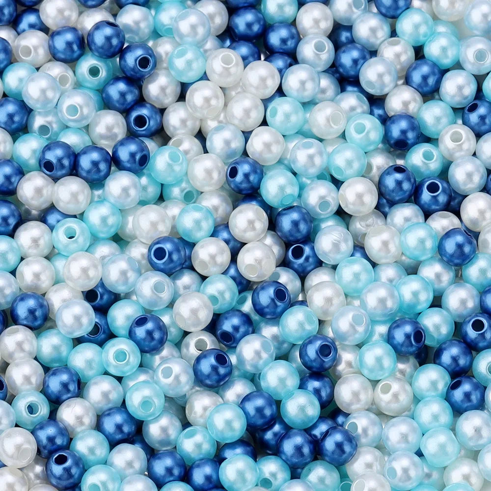 A close-up of small imitation pearl beads in various shades of blue and white scattered on a surface.