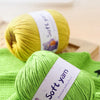 A ball of bright lime green soft yarn is displayed on a green knitted fabric.