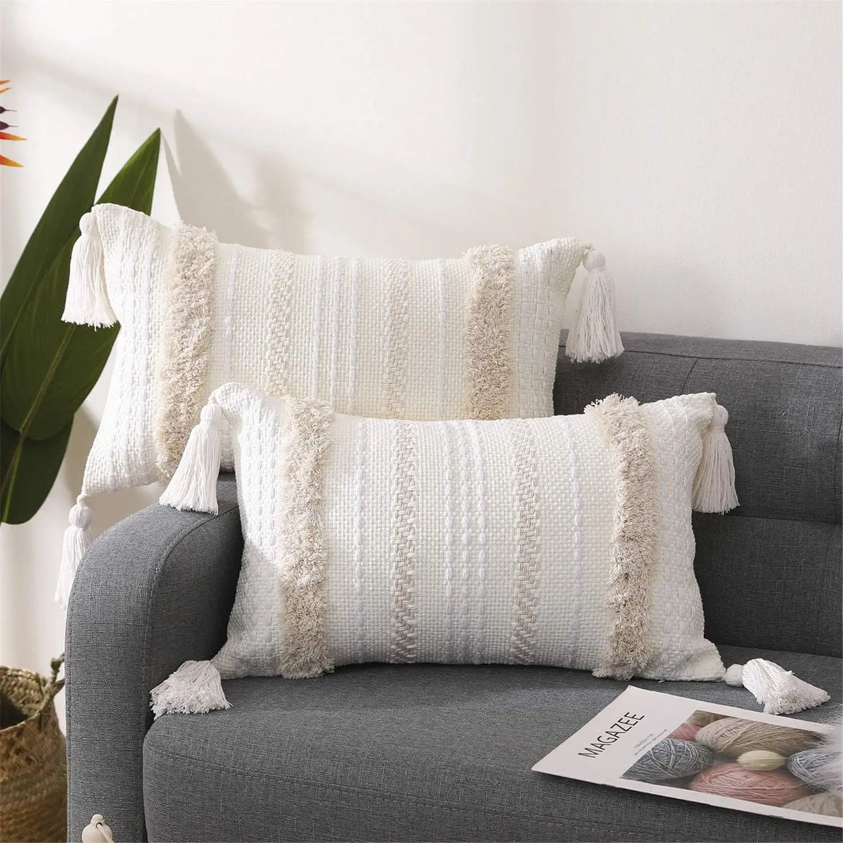 White boho tufted throw pillow cover with cream tassels resting on a gray sofa.