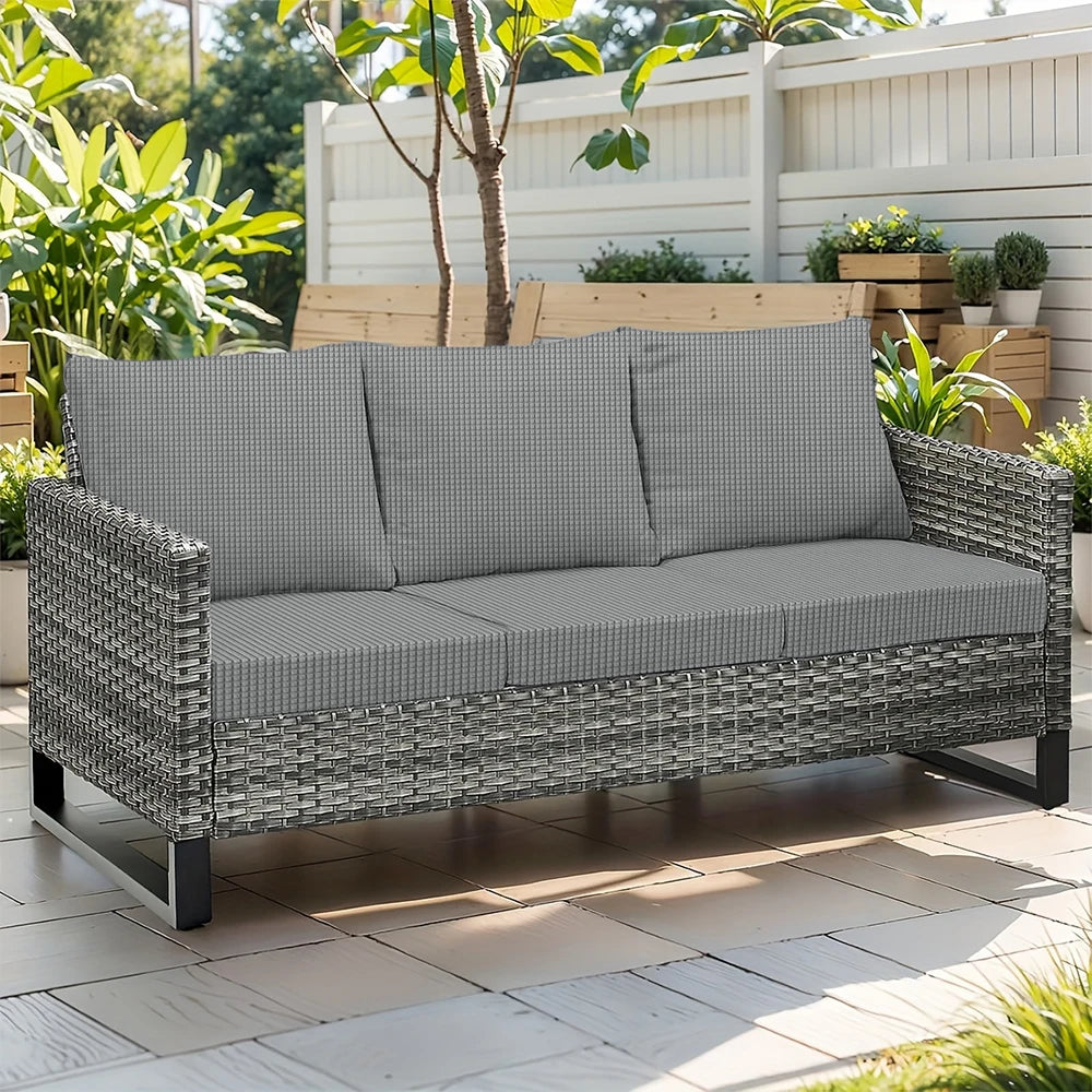 Gray woven outdoor sofa seat slipcover placed on a wooden deck with greenery in the background.