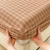 Hands holding a fitted sheet with a striped brown and beige pattern.