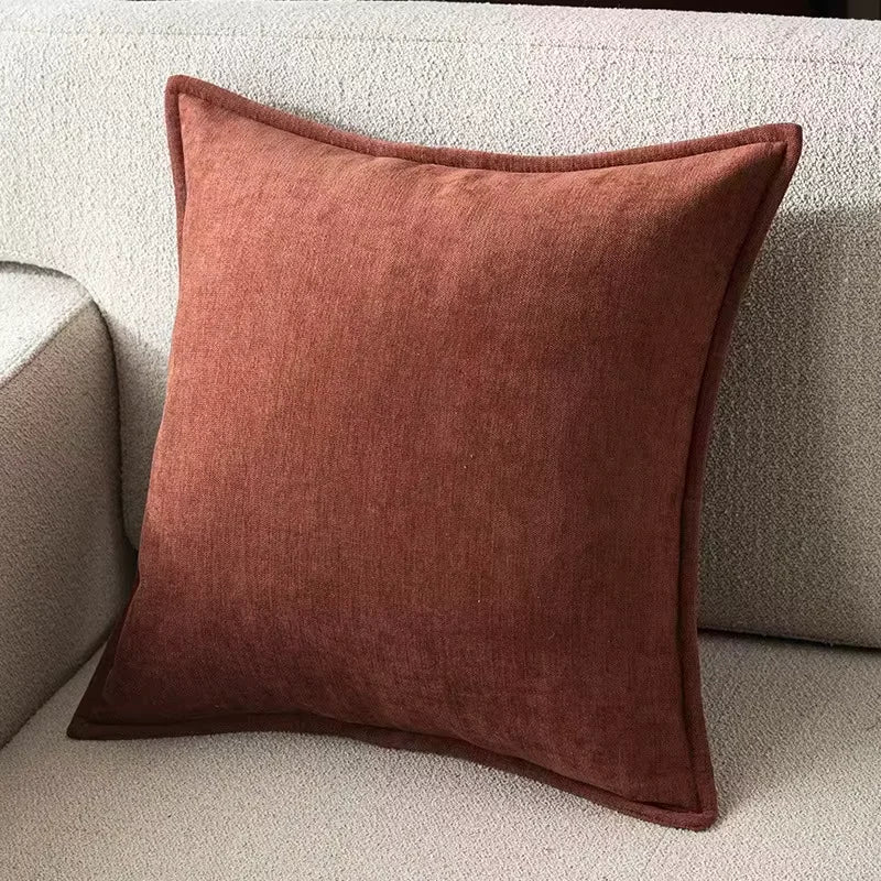A square, rust-colored chenille throw pillow resting on a light beige sofa.
