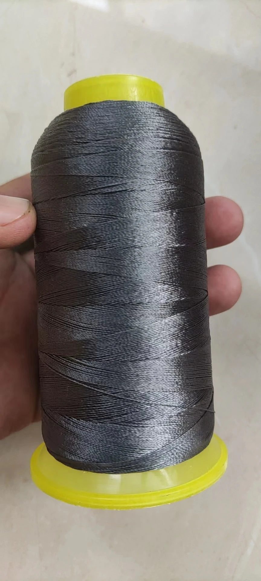 A spool of gray high tenacity polyester sewing thread with a yellow plastic core and base.