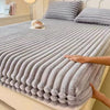 A close-up of thick gray winter fitted bed sheets folded on a bed, with a hand touching the fabric.