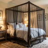 A large outdoor mosquito netting draped over a wooden bed frame in a bedroom setting.
