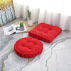 Two red tufted corduroy floor seat cushions resting on a light gray patterned rug near a window.