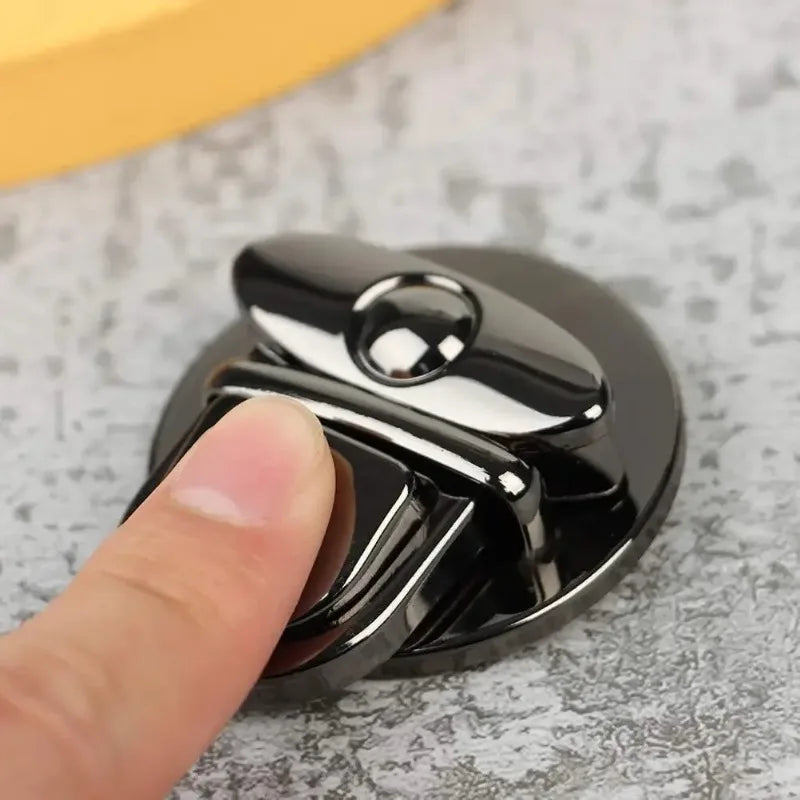 A hand is pressing a black metal twist lock mechanism used for securing bags or cases.