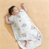 A baby is lying on a light yellow surface wearing an ultra-soft baby sleeping bag with colorful embroidered patterns.
