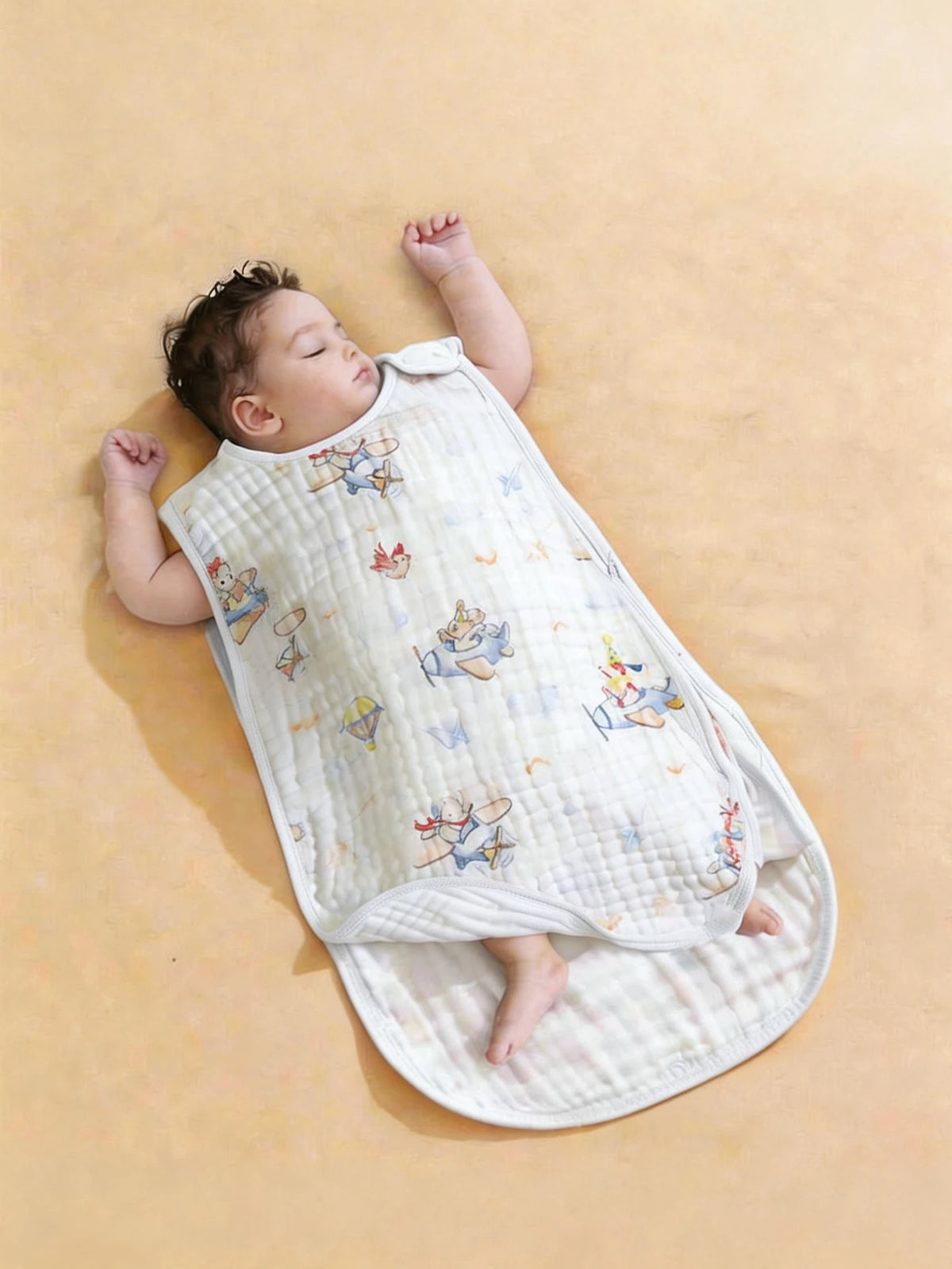 A baby is lying on a light yellow surface wearing an ultra-soft baby sleeping bag with colorful embroidered patterns.