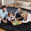 A family is playing with a colorful wooden puzzle on a dark rug in a living room.