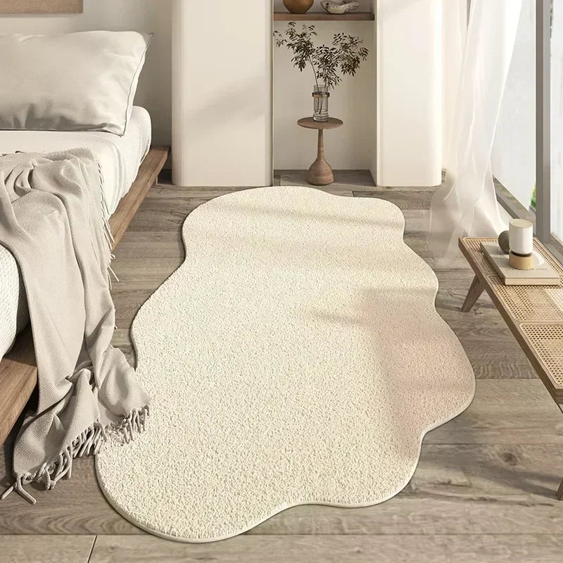 A cream colored irregular plush area rug placed on a light wood floor in a bright room.