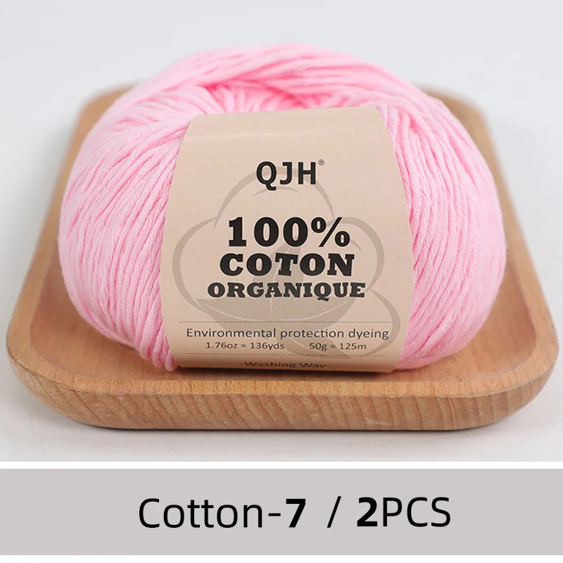 Pink QJH 100% organic cotton yarn skein displayed on a wooden board.