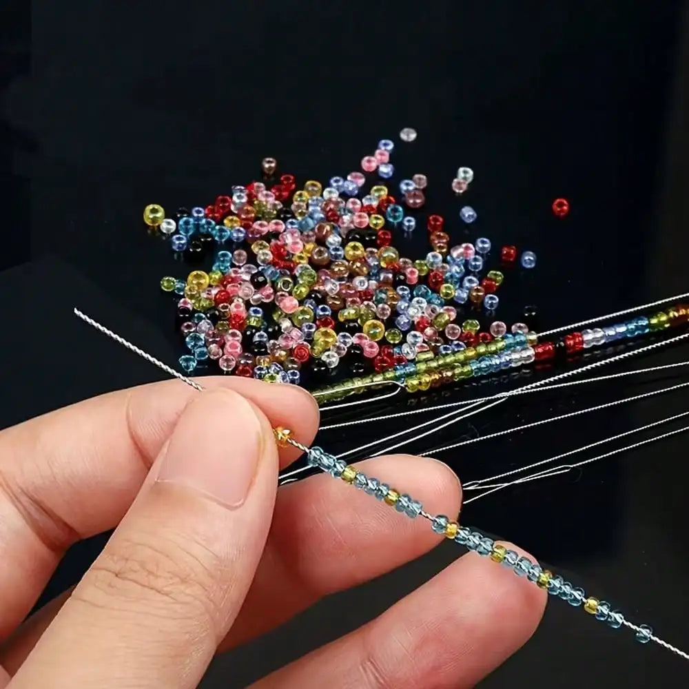 A hand holds a precision beading needle set with various colored beads and threads for jewelry making.