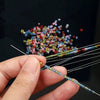 A hand holds a precision beading needle set with various colored beads and threads for jewelry making.