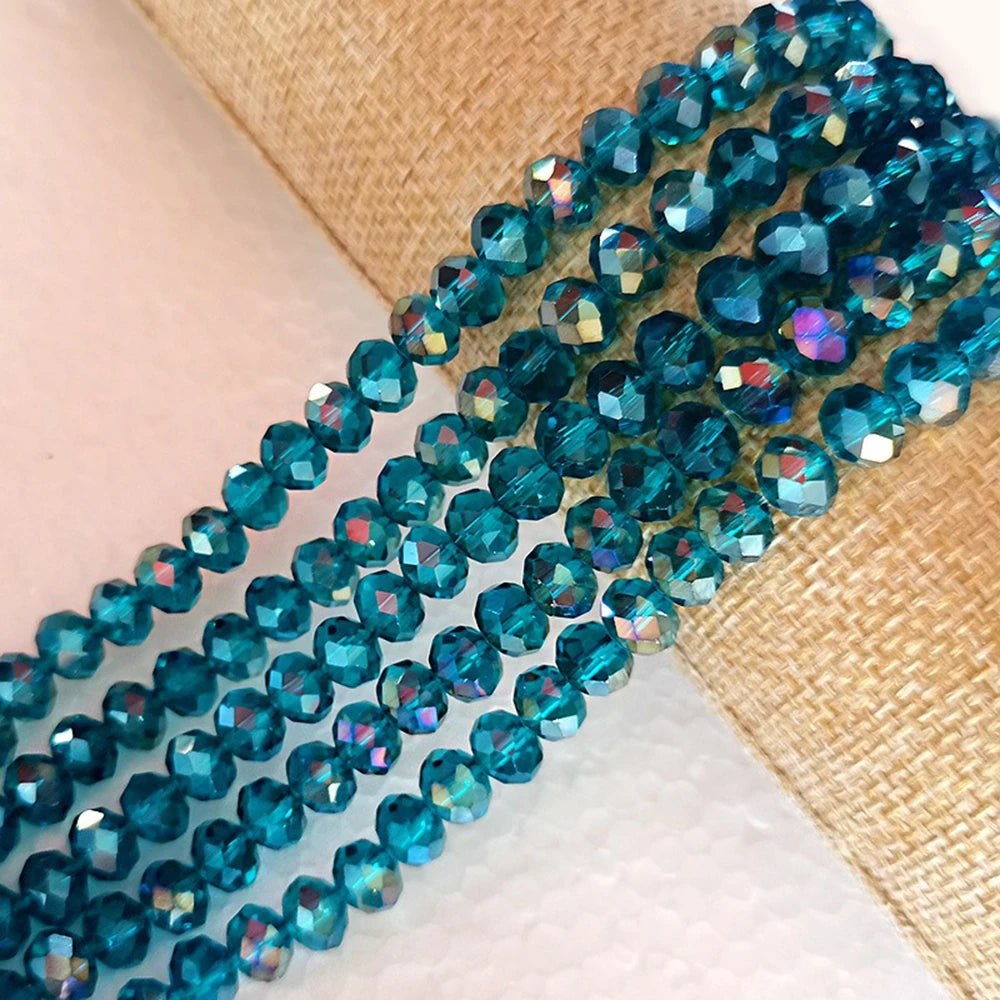 A strand of faceted blue-green glass beads is laid across a beige woven fabric.