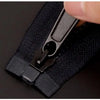 A hand is shown manipulating a black universal zipper repair kit with replacement sliders on a dark fabric.