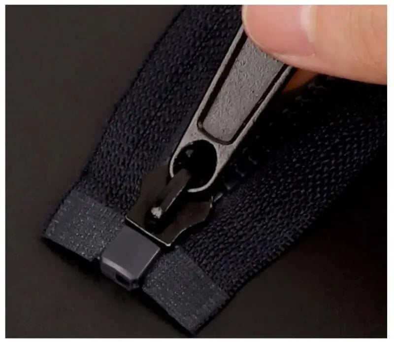 A hand is shown manipulating a black universal zipper repair kit with replacement sliders on a dark fabric.
