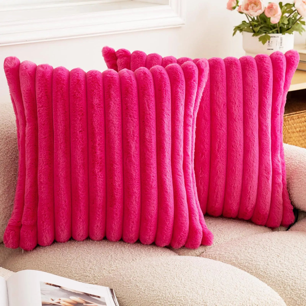 A bright pink square faux rabbit fur cushion cover resting on a beige sofa.