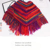 A hand-knitted poncho made from rainbow color gradient wool yarn with fringed edges.