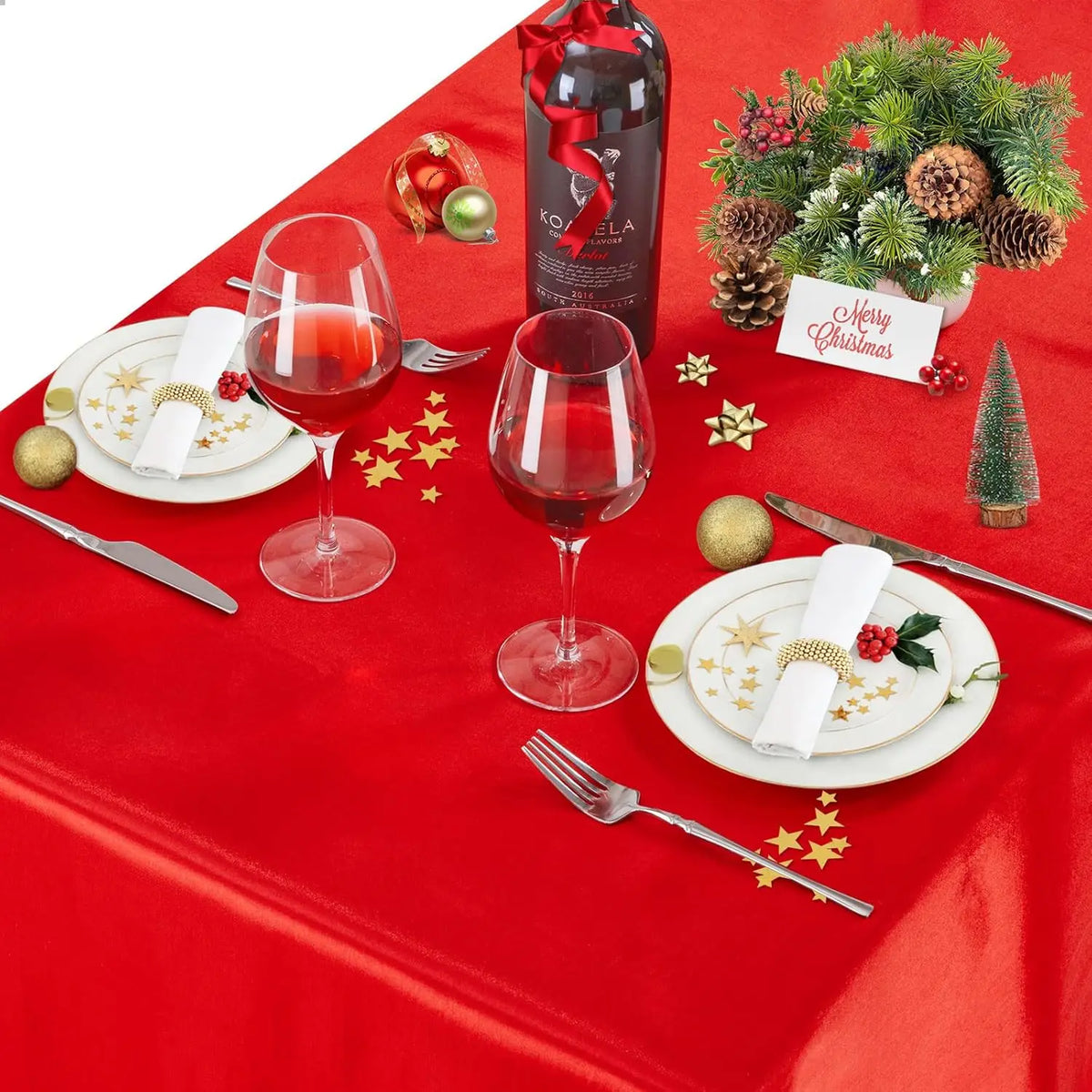 A red satin tablecloth set for elegant dining featuring wine glasses, cutlery, and Christmas decor.