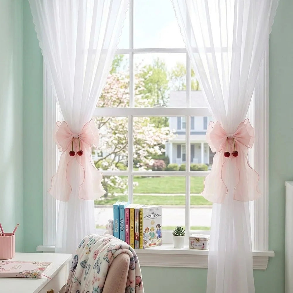 A pair of pink French ribbon bow curtain tiebacks hanging on a window with sheer white curtains.