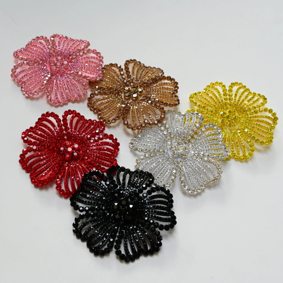 A collection of nine colorful rhinestone flower applique patches in shades of pink, gold, yellow, red, and black.
