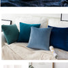 A collection of velvet throw pillows in shades of teal, blue, and gray on a white sofa.