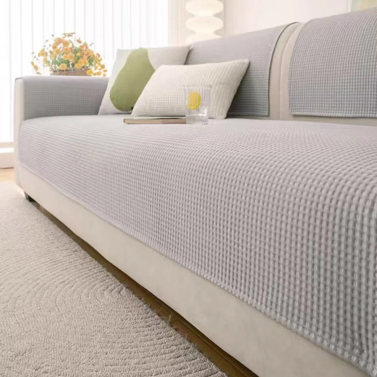 A light gray machine washable anti-slip sofa slipcover with decorative pillows and a white textured rug.