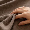 A hand gently touches a textured, brown quilted fabric, likely a non-slip sofa cover.