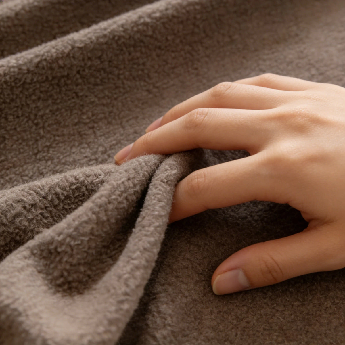 A hand gently touches a textured, brown quilted fabric, likely a non-slip sofa cover.