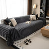 A dark gray bohemian striped sofa cover draped over a sofa in a bright room.