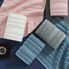 A set of four textured face towels in pink, white, and blue tones are displayed on a dark surface.