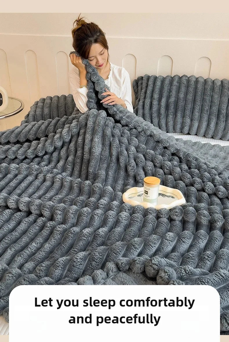 A gray cozy flannel blanket is draped over a bed, with a woman looking down at it.
