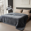 A gray flannel blanket is draped on a bed while water pours from a metal pitcher onto the fabric.