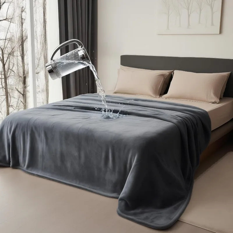 A gray flannel blanket is draped on a bed while water pours from a metal pitcher onto the fabric.