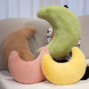 Three moon-shaped throw pillows in shades of green, brown, and pink resting on a light sofa.