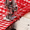 A close-up of a sewing machine with a rolled hem foot being used on red and white checkered fabric.