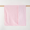 A pink fleece swaddle blanket with a dimpled texture is hanging on a wooden rod.
