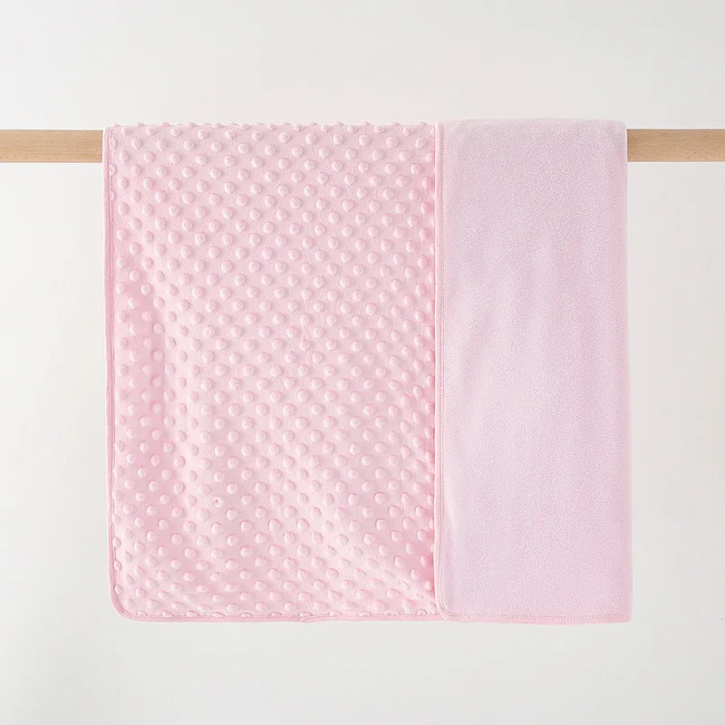 A pink fleece swaddle blanket with a dimpled texture is hanging on a wooden rod.