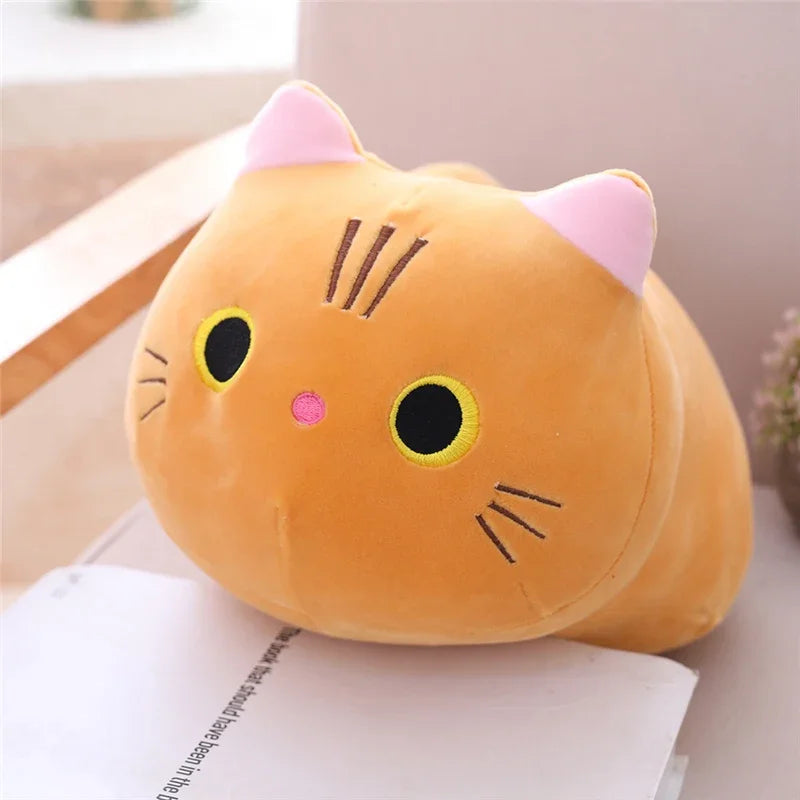 An orange soft cat plush pillow cushion with pink ears and yellow eyes resting on a white surface.