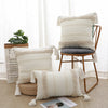 A cream and beige boho tufted throw pillow cover with tassels resting on a wooden chair.