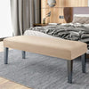 A beige velvet bench slipcover with secure straps placed on a gray striped rug in a bedroom setting.