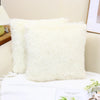A fluffy white faux fur throw pillow resting on a white surface.