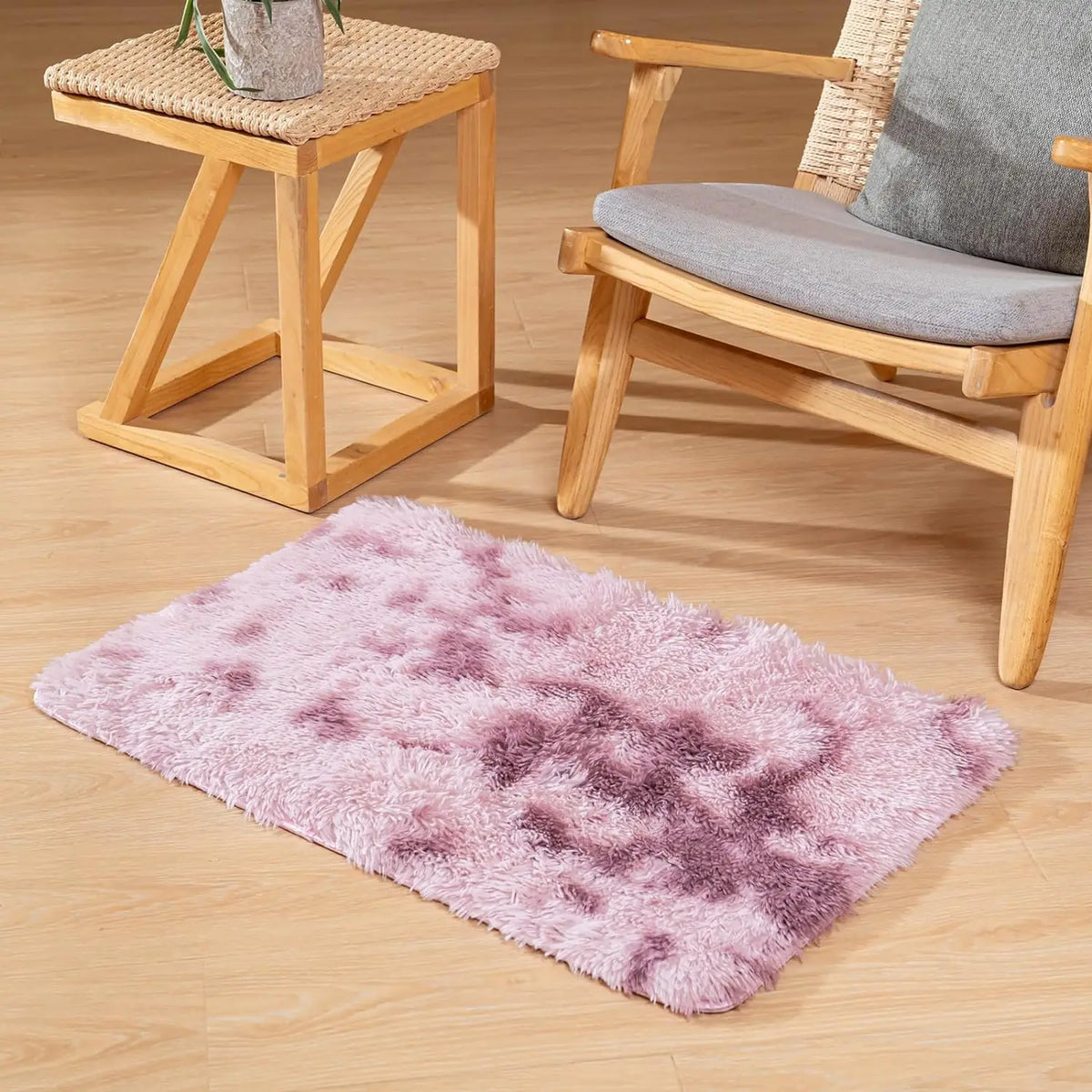 A fluffy pink and purple area rug placed on a light wooden floor next to a wooden side table and a wooden chair.