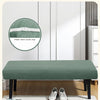 A green stretch jacquard dining bench cover placed on a wooden table with white shoes nearby.