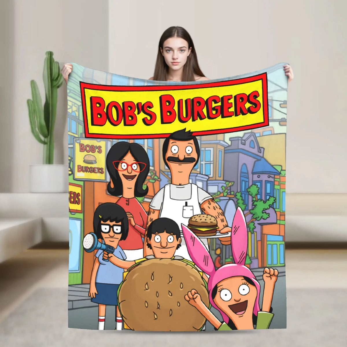 A person holding a large throw blanket featuring characters from Bob's Burgers and other cartoon figures.