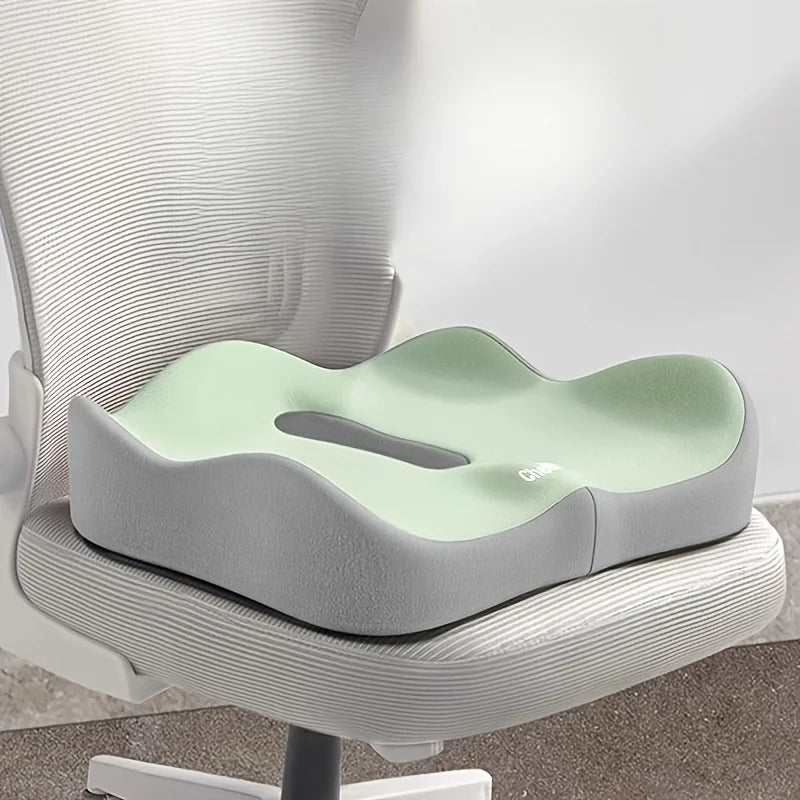 A light green ergonomic memory foam seat cushion placed on a gray office chair.